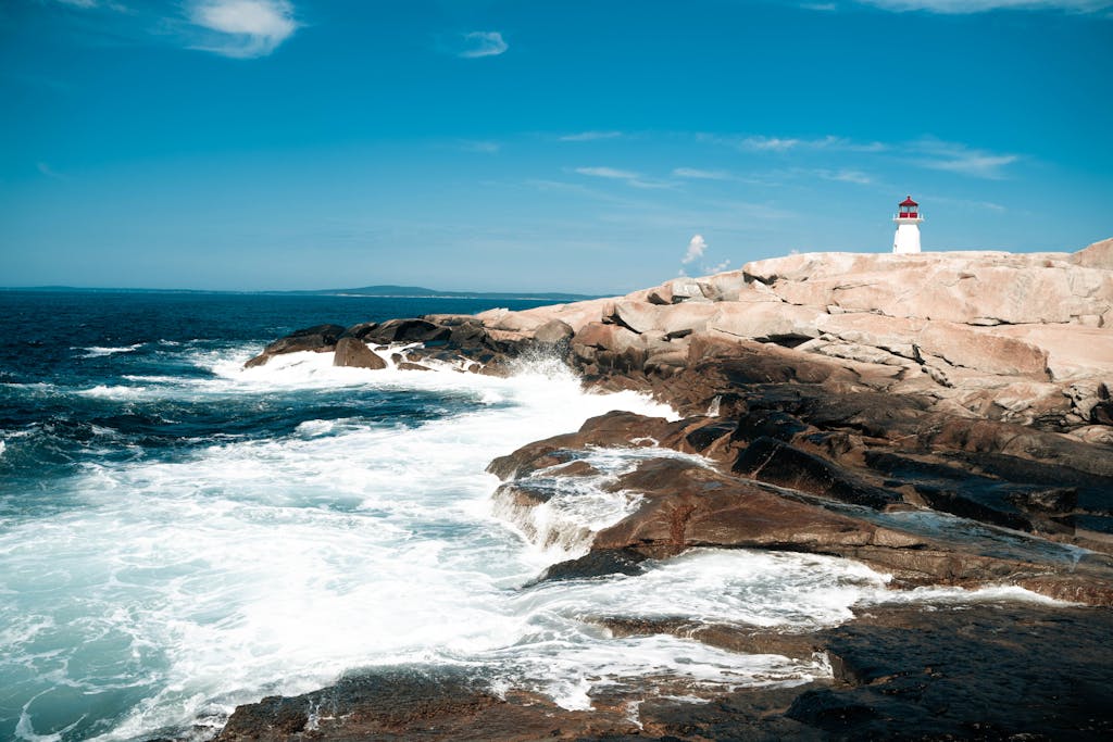 Dramatic landscape of Peggys Cove Lighthouse with crashing waves on a sunny day.