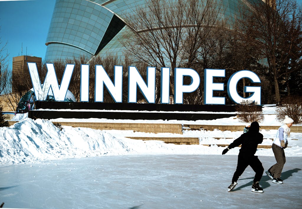 People ice skating in front of the iconic Winnipeg sign on a sunny winter day.